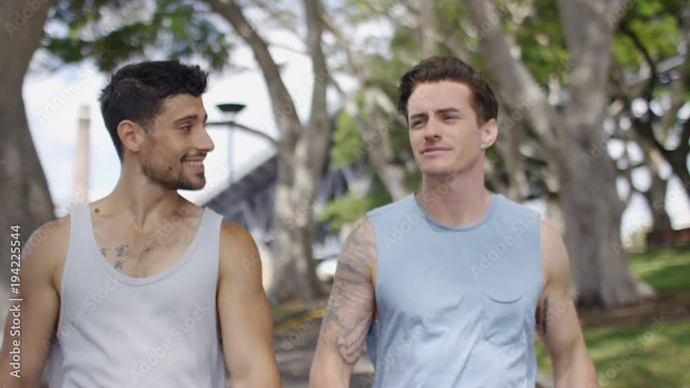 Two male friends walking and talking through a park Two male friends walking and talking through a park