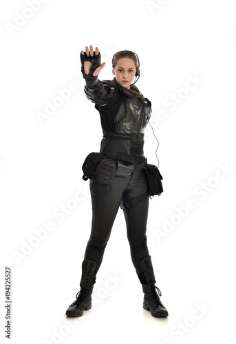 full length portrait of female soldier wearing black tactical armour with arms raised, isolated on white studio background.