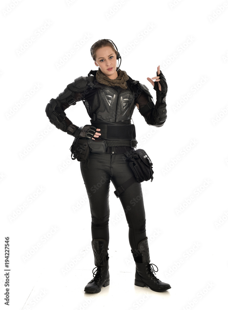 full length portrait of female  soldier wearing black  tactical armour with arms raised, isolated on white studio background.