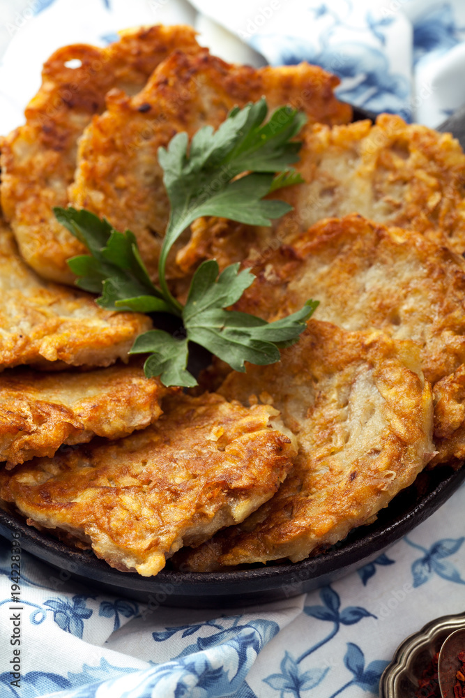 Potato latkes traditional jewish pancakes with sour cream, parsley, dry red pepper flakes and mint sauce. Background, white napkin with blue flowers. Hannukah celebration dish concept. Close up.