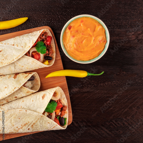 Mexican burritos with cheese salsa, chili peppers, and copyspace, square photo
