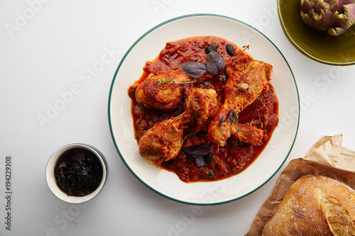Chicken legs cooked in italian cacciatore style with tomato sauce and fresh basil on white table photo