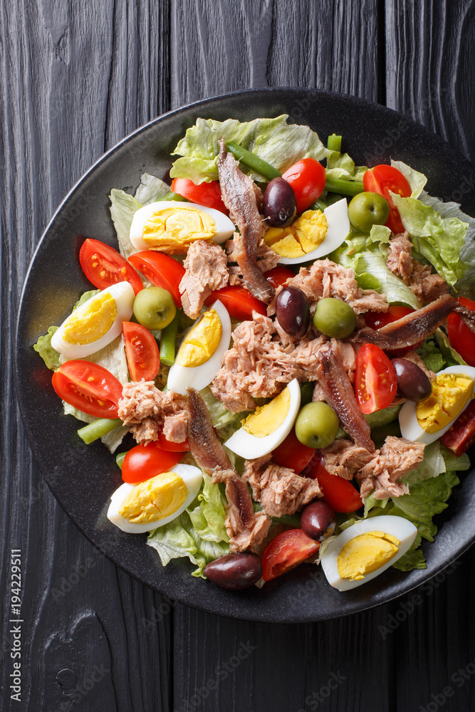 nicoise salad of tuna, anchovies, eggs, tomatoes, green beans, olives and lettuce close-up on a plate. Vertical top view