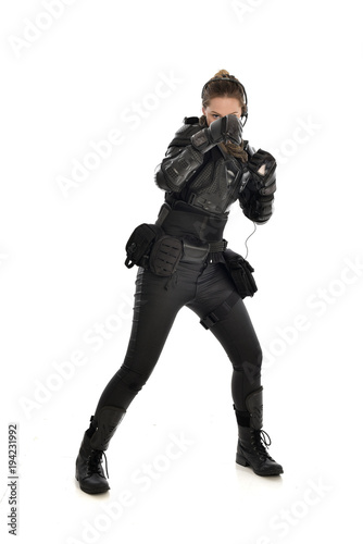full length portrait of female soldier wearing black tactical armour with arms raised, isolated on white studio background.
