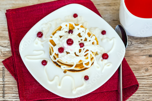 Fresh baked pancakes for Breakfast in a white plate, decorated with sour cream and cranberries, with berry fruit in a Cup,