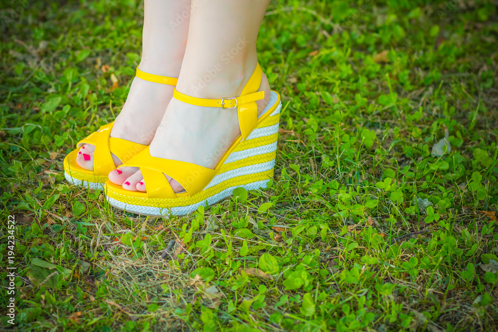 women's feet in yellow summer sandals from open-topped on a tankette. Trendy sexy shoes .Pair of vintage female  sandals isolated on green grass. Female  platform shoes. Copy space