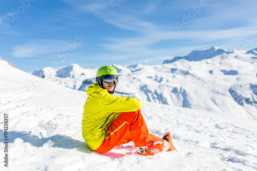 Photo of sportive man wearing helmet wearing yellow jacket sitting on snowy slope