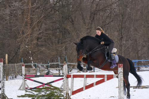 A girl on a horse jumps over the barrier. Training girl jockey riding a horse. A cloudy winter day.