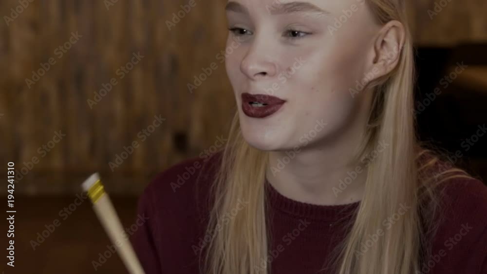 Portrait of blond woman, who is talking to her frends. Young lady is sitting and shaking the pencil in her hand to agree with the speaker, smiling wide by her beautiful face with bordo lipstick on the Portrait of blond woman, who is talking to her frends. Young lady is sitting and shaking the pencil in her hand to agree with the speaker, smiling wide by her beautiful face with bordo lipstick on the