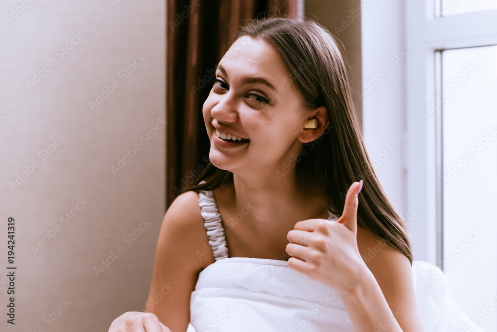 happy woman with ear plugs in her ears sits on the bed happy woman with ear plugs in her ears sits on the bed