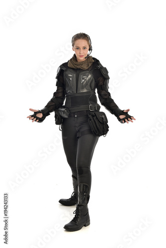 full length portrait of female soldier wearing black tactical armour with arms raised, isolated on white studio background.