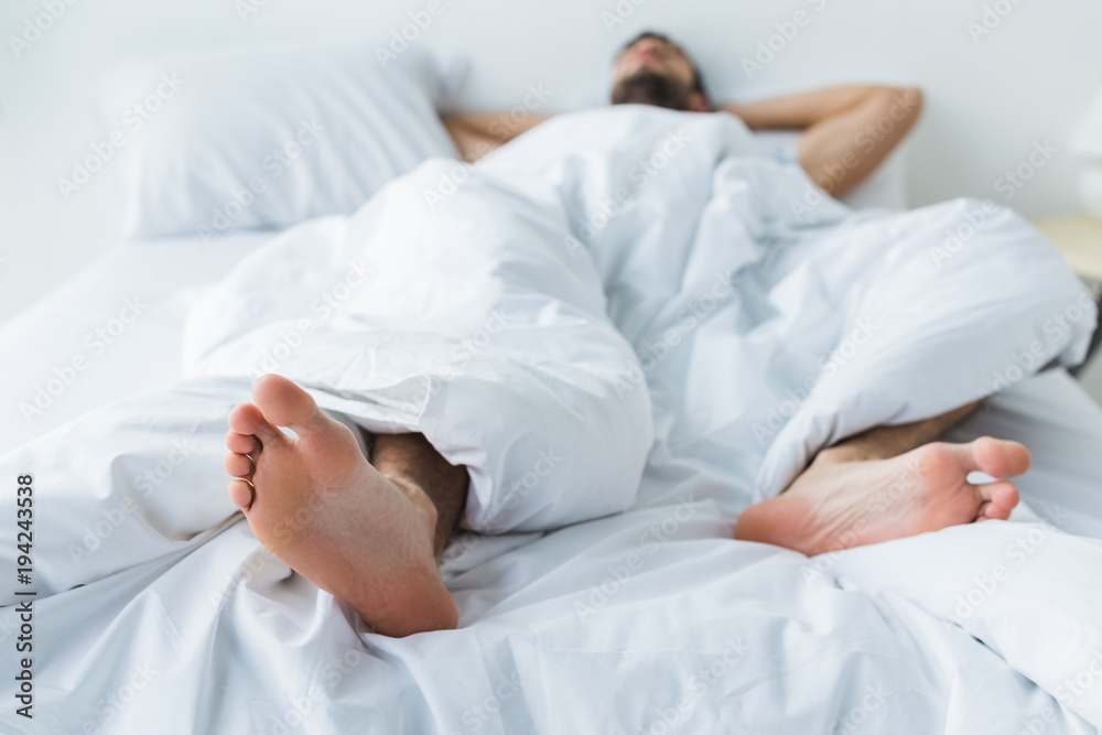 selective focus of man sleeping on bed, feet on foreground selective focus of man sleeping on bed, feet on foreground