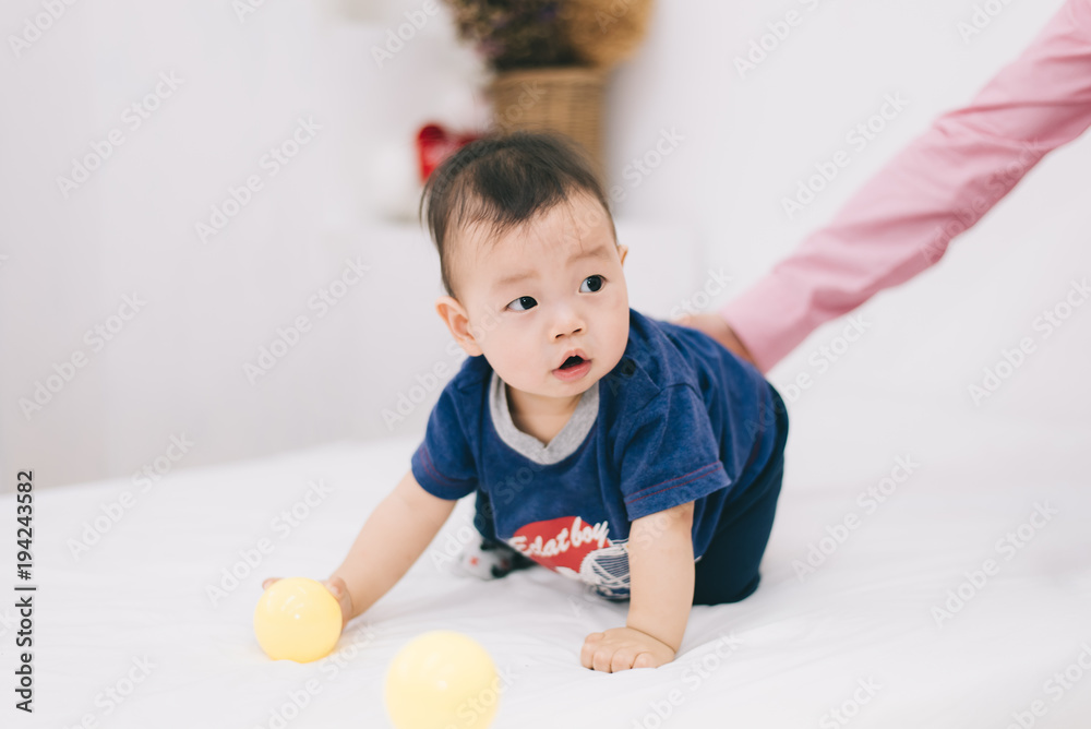 Adorable asian chubby baby boy playing a plastic ball in white living room. He feeling fun and looking to his mother and father , Happy family time on vacation concept Adorable asian chubby baby boy playing a plastic ball in white living room. He feeling fun and looking to his mother and father , Happy family time on vacation concept