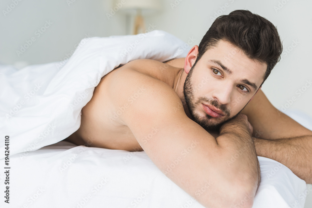 handsome bearded man lying on white bed