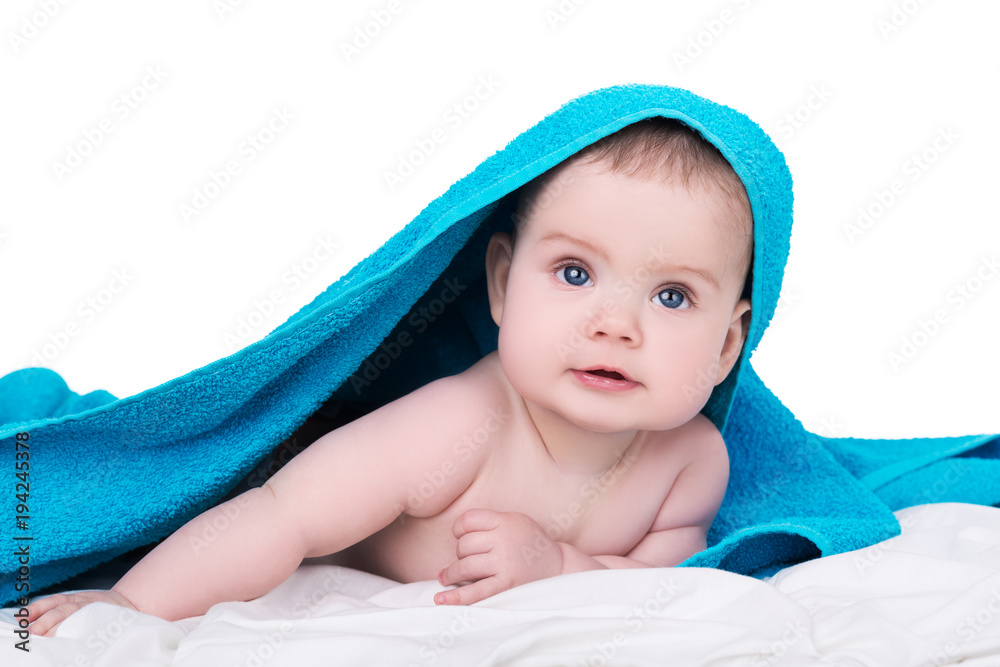 Surprised smiling baby with big blue eyes lying on belly under the blue towel after shower, isolated on white background Surprised smiling baby with big blue eyes lying on belly under the blue towel after shower, isolated on white background