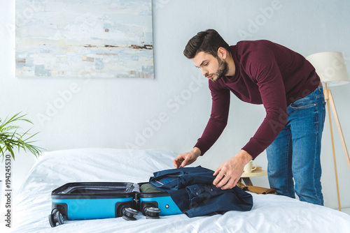 handsome man packing clothes into travel bag for trip