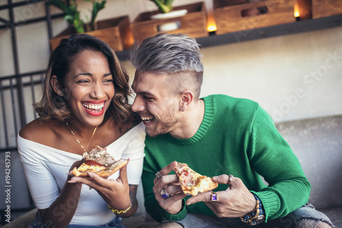 Картината върху платно Mixed race couple eating pizza in modern cafe