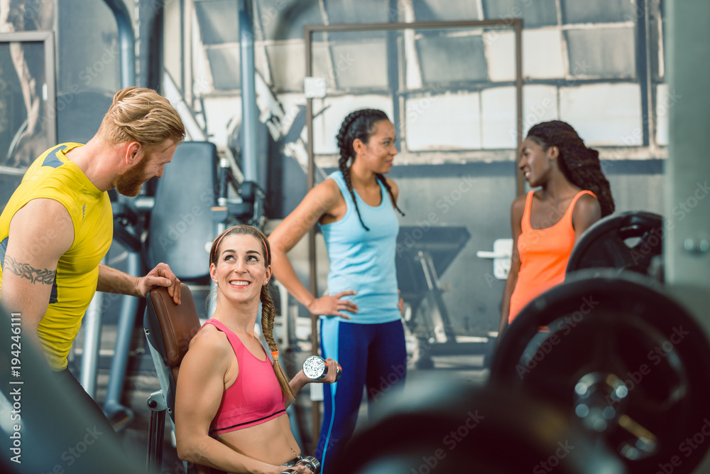 Side view of a handsome personal trainer guiding his female client while exercising with a small dumbbell for toned arms at the gym Side view of a handsome personal trainer guiding his female client while exercising with a small dumbbell for toned arms at the gym