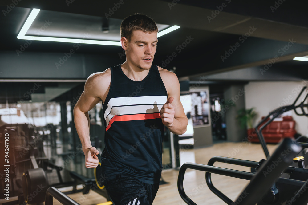 Horizontal shot of Caucasian athletic man running in a modern gym on a treadmill doing cardio exercises. Sport, fitness, healthy life and people concept.
