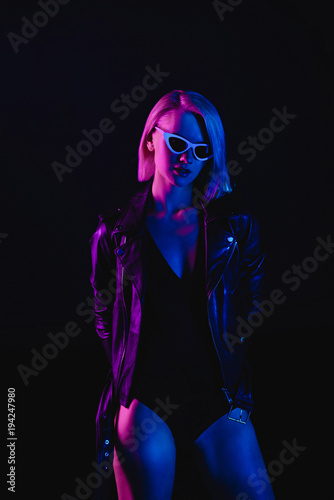 fashionable girl posing in black leather jacket and sunglasses, isolated on black