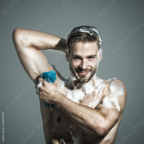 Relax and hygiene, spa and beauty, healthcare - handsome man washing with sponge in shower. He is smiling from good mood. Bodybuilder, sexy strong man washing with foam sponge after workout.