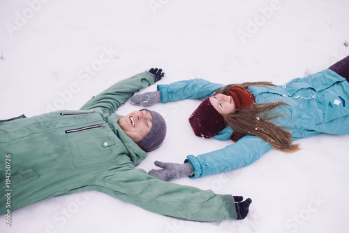 Happy Young Couple having fun in Winter Park. young man and woman lying on the snow. Family Outdoor. people, season, love and leisure concept