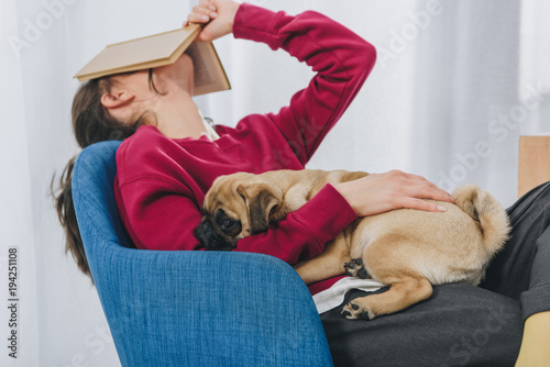 Pretty lady hugging pug and covering her face with book