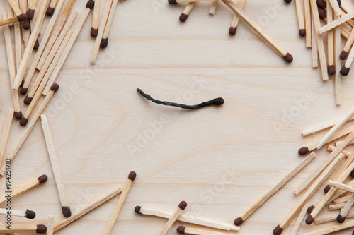 wooden unburned matches with black heads scattered against a light brown wood. lonely burnt match in the center