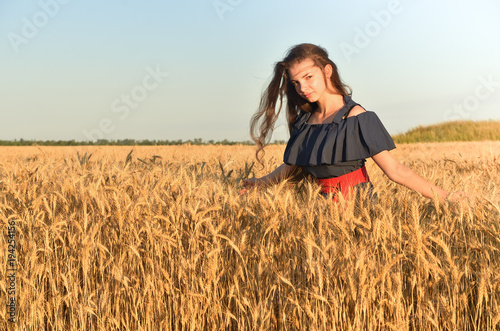 A woman with long hair in dress stands among the wheat flocks in the field