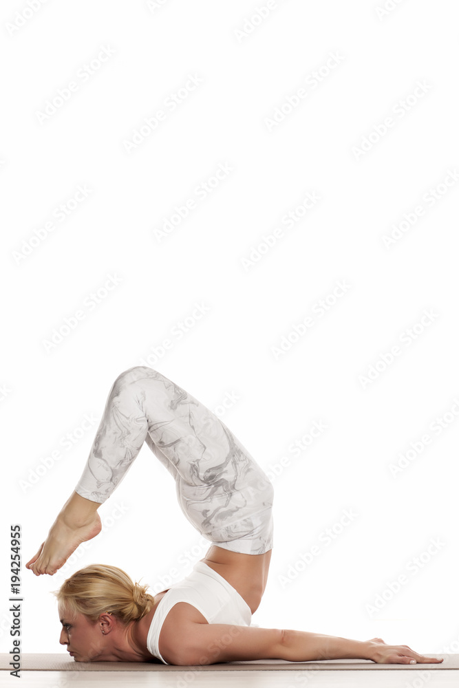 Yoga, sport, training and lifestyle concept - Young blonde woman doing yoga exercise. Portrait of young beautiful woman in white sportswear doing yoga practice.Chin stand/ Ganda bherudasana Yoga, sport, training and lifestyle concept - Young blonde woman doing yoga exercise. Portrait of young beautiful woman in white sportswear doing yoga practice.Chin stand/ Ganda bherudasana