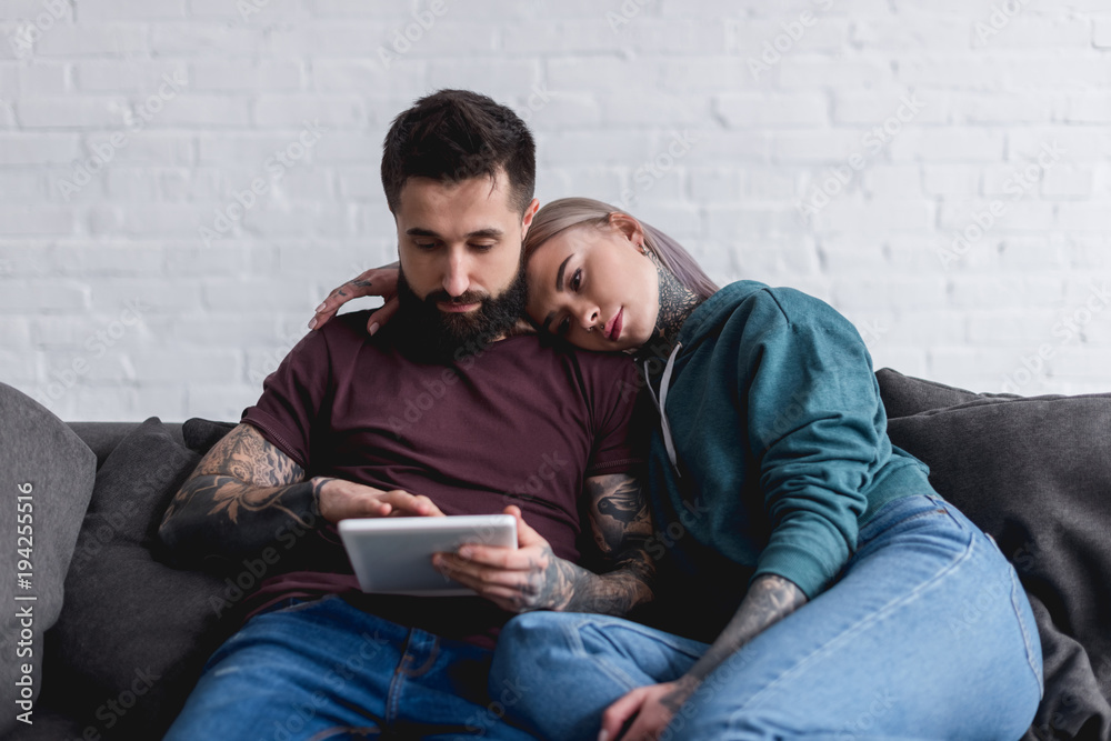 tattooed couple watching something at tablet at home