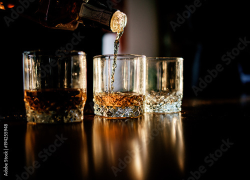 Fotografie, Obraz Man pours whisky in the glasses standing before a wooden table