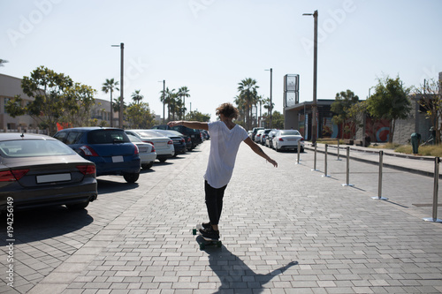 A young man in a white t-shirt riding a skateboard on the street. © kanashkin