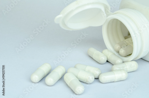 Capsule drugs pills spilled from white bottle on white background