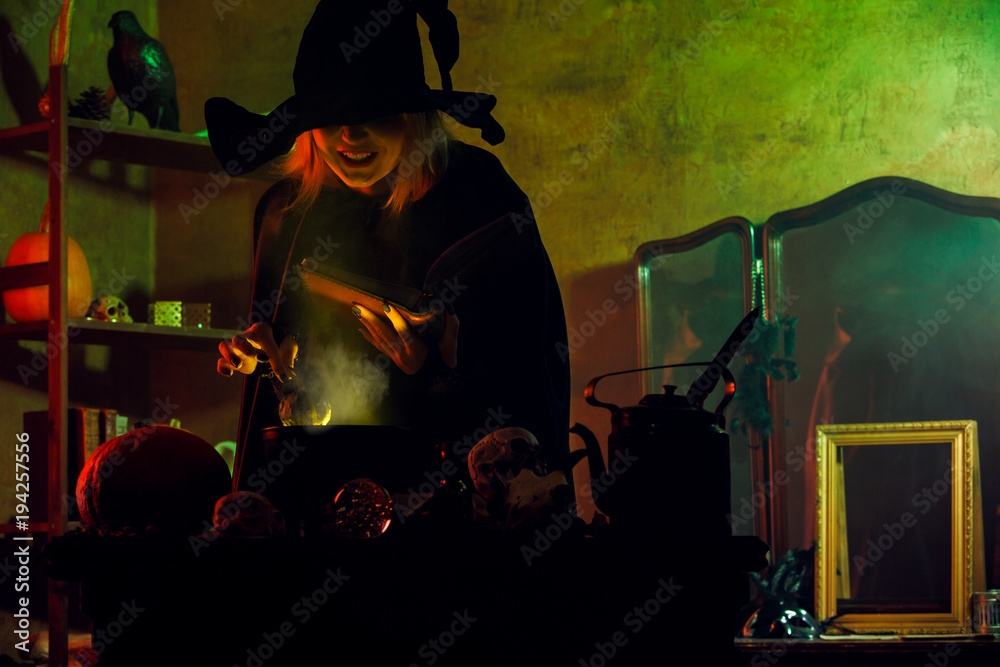 Image of witch in black hat reading spell over pot of green steam