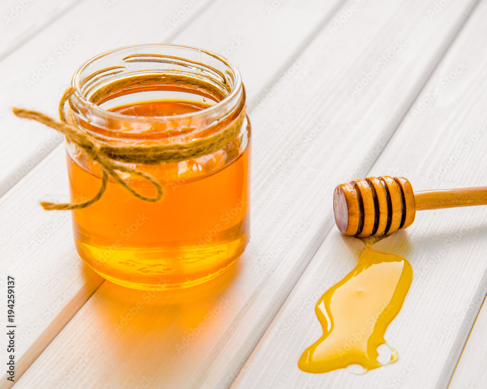 Glass jar with honey and dipper on white wooden table background Glass jar with honey and dipper on white wooden table background