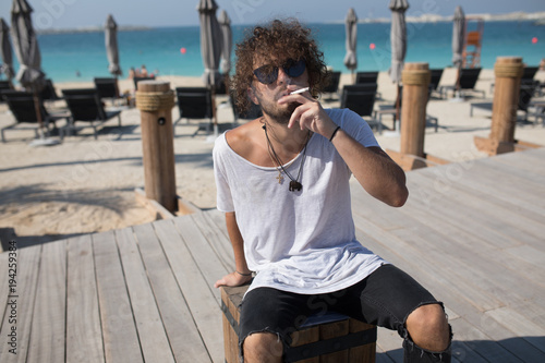 Stylish man sitting near the beach and smoking.