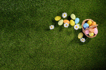 above top view of multi colored painted easter eggs on the green grass with springtime daisy flowers