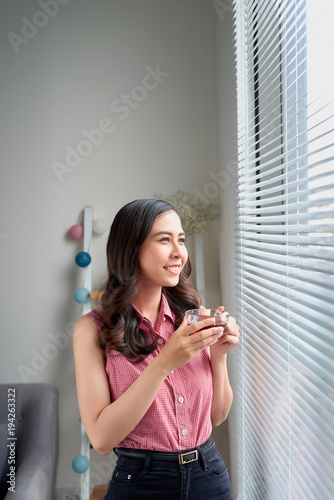 Young woman taking a tea break standing by the office window.
