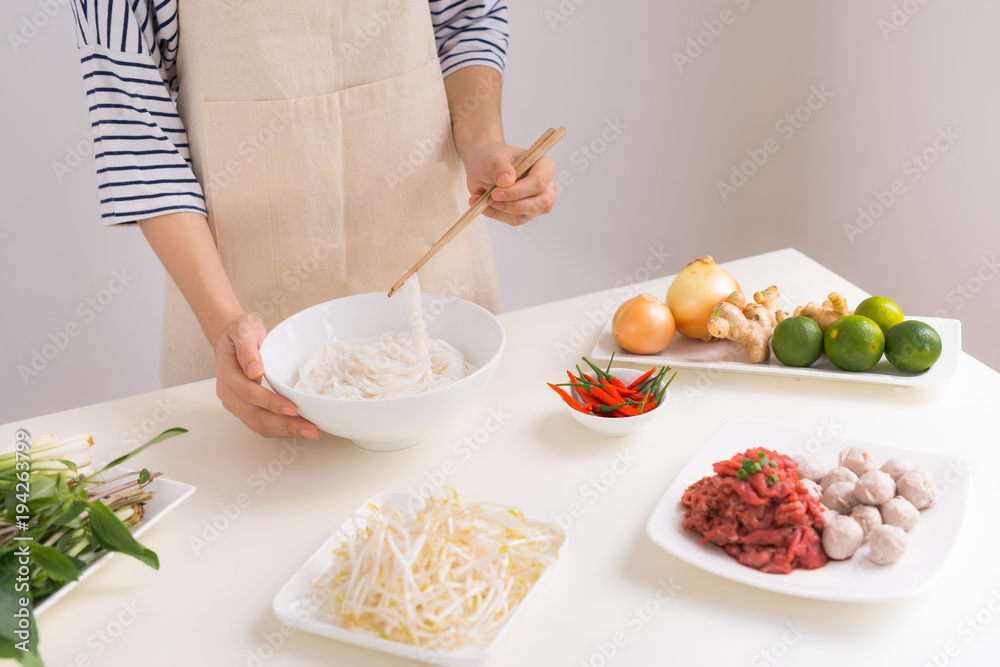 Female chef prepare traditional Vietnamese soup Pho bo with herbs, meat, rice noodles