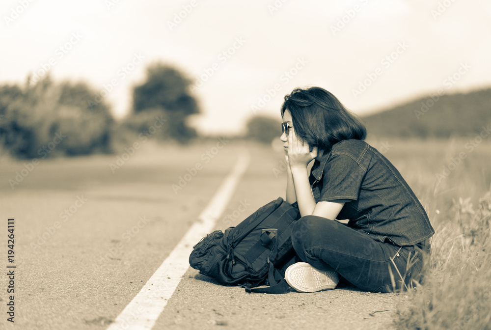 Woman sit with backpack hitchhiking along a road in countryside Woman sit with backpack hitchhiking along a road in countryside