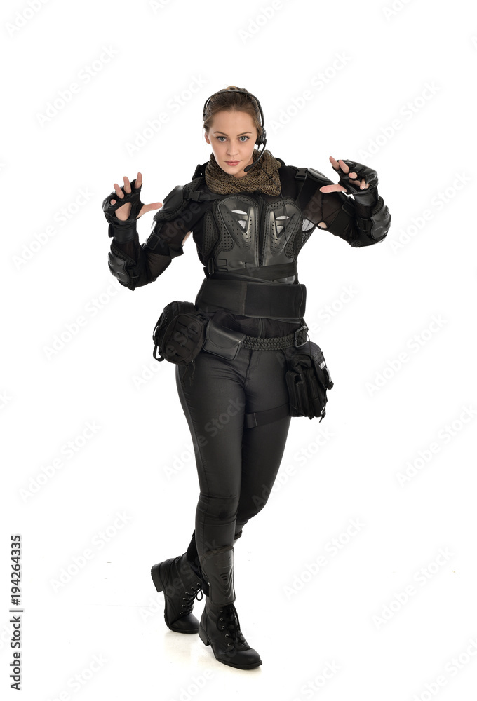 full length portrait of female soldier wearing black tactical armour with arms raised, isolated on white studio background. full length portrait of female soldier wearing black tactical armour with arms raised, isolated on white studio background.