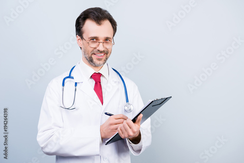 Clinical occupation medico equipment professional qualified doctor holding clipboard writing prescription with pen wearing formalwear white coat red tie isolated on gray background copy-space