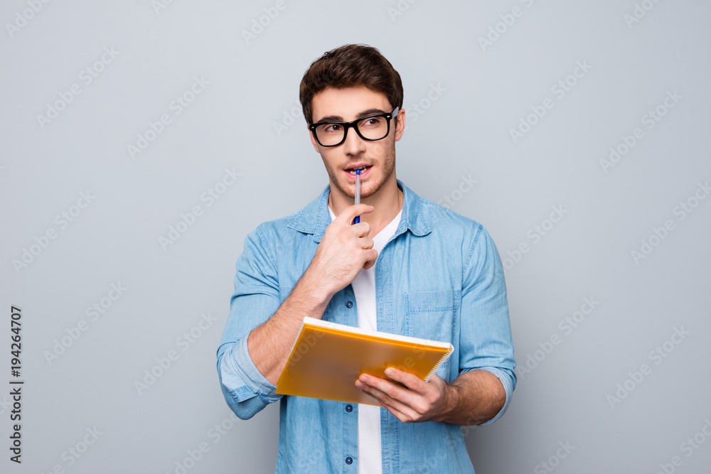 Handsome, attractive, glad, positive, funny guy in glasses with wide open mouth finally found a solution how to make exercise, having raised pen and notebook in hands, isolated on grey background Handsome, attractive, glad, positive, funny guy in glasses with wide open mouth finally found a solution how to make exercise, having raised pen and notebook in hands, isolated on grey background