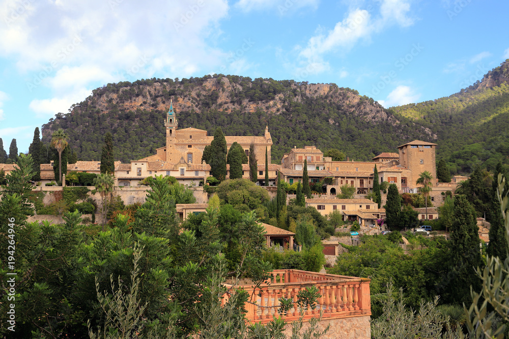 View of Valldemossa village on Mallorca with the Royal Charterhouse of Valldemossa among the green trees with a wooded mountain in the background