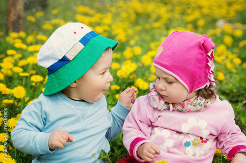 Little boy and girl in hats sitting on the field with soft toys in summer