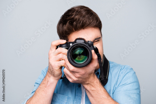 Portrait of guy in jeans shirt looking at photo camera, shooting photographs during excursion, making photosession over gray background photo