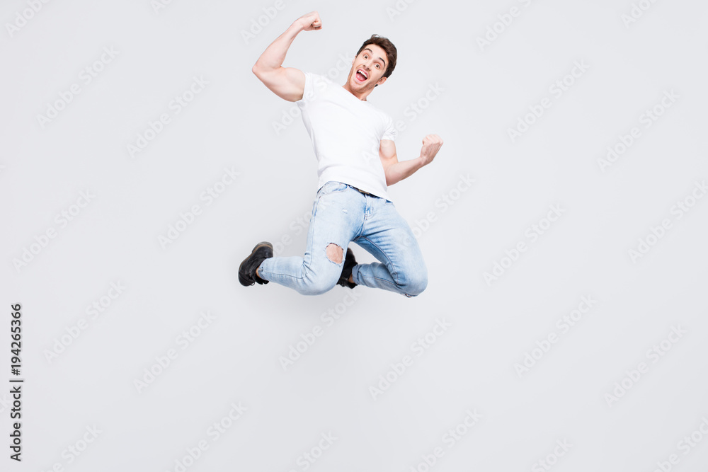Full-size full-length portrait of carefree restless cheerful joyful stylish trendy guy with modern haircut dressed in denim trousers boots white t-shirt raising fists isolated on gray background
