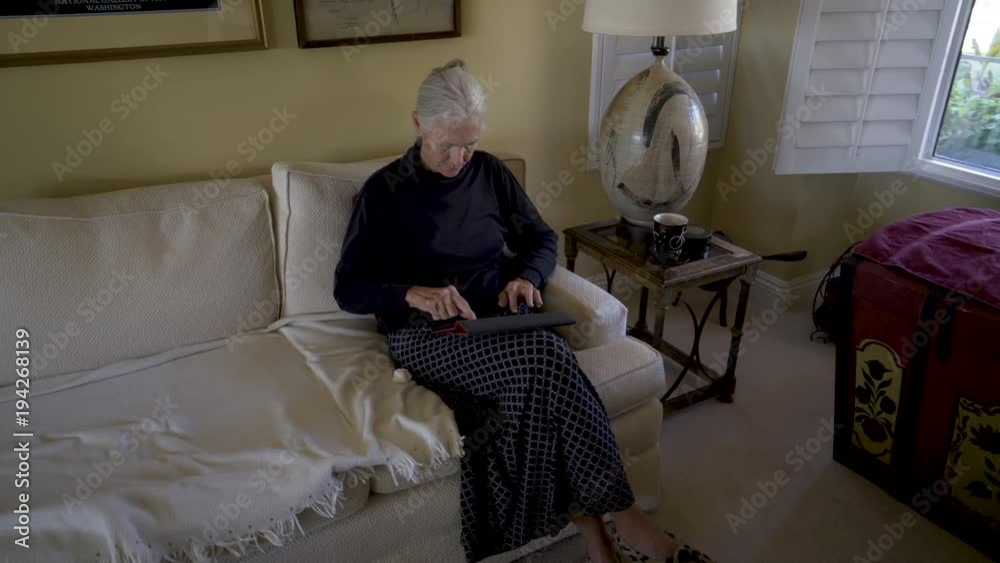 Steadicam motion to the right around a pretty senior woman in a living room with coffee looking at a tablet computer. Steadicam motion to the right around a pretty senior woman in a living room with coffee looking at a tablet computer.