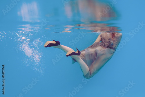 Amazing beautiful art surreal portrait of woman's legs in violet shoes underwater in the swimming pool